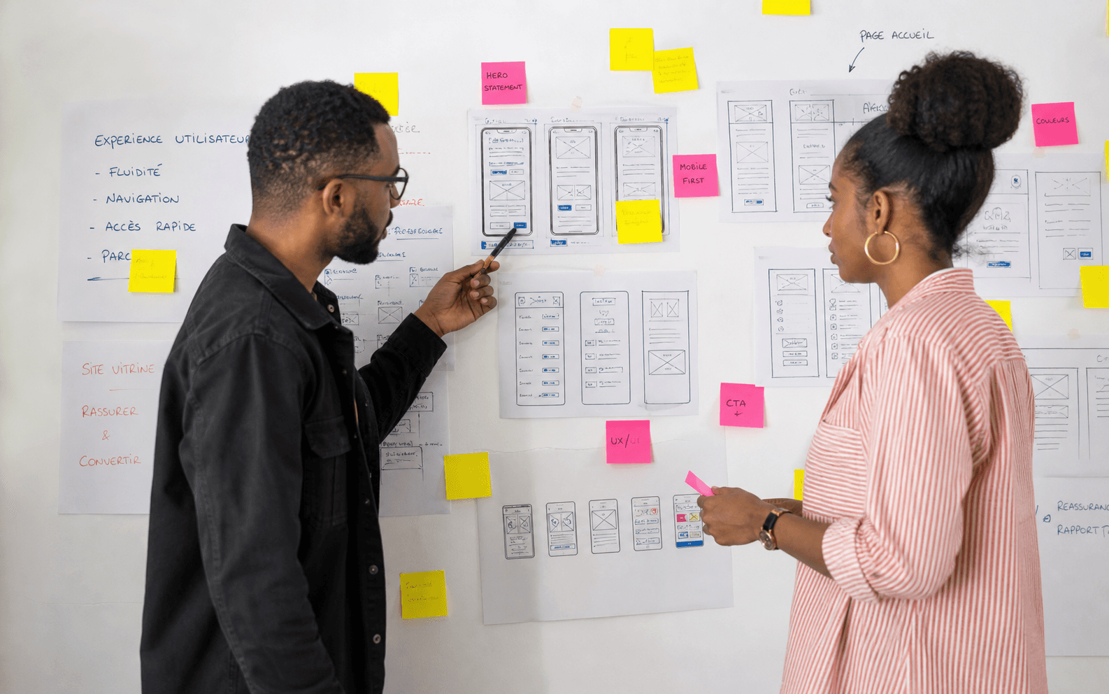 Deux designers mahorais en atelier de refonte web devant un mur de post-its et de wireframes papier
